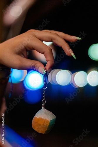 Foto Vertical closeup of a hand holding a Rubik's cube keychain with bokeh lights in