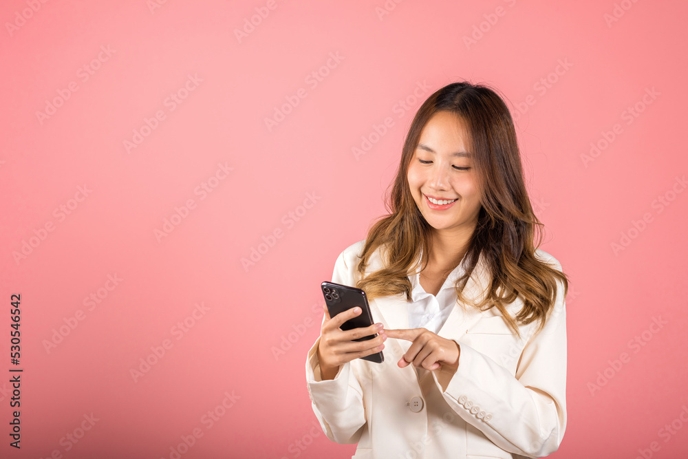 Portrait Asian happy beautiful young woman smile making finger pointing on screen smartphone in hand shopping online application looking to screen, studio shot isolated pink background with copy space Portrait Asian happy beautiful young woman smile making finger pointing on screen smartphone in hand shopping online application looking to screen, studio shot isolated pink background with copy space