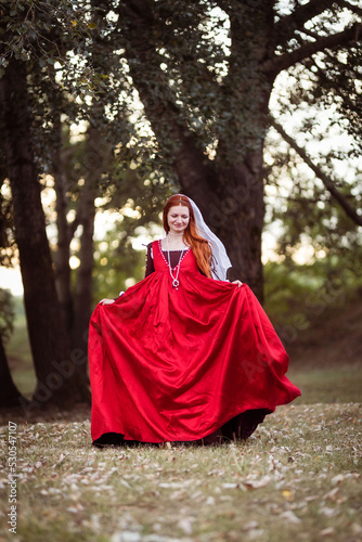 Portrait of a red-haired woman in a historical costume of the 15th century - a red silk dress in the fashion of Venice. Lady running through the forest