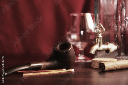 Moody man's table in cabinet with cognac, smoking pipe, matches, bottle. Leisure activity and evening relax concept