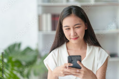 Beautiful Asian businesswoman using a smartphone to contact customers reply to chat Transact on social media applications in the office with a smiling face.