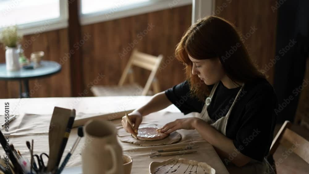 A red-haired potter girl cuts a circle from a piece of clay using special tools