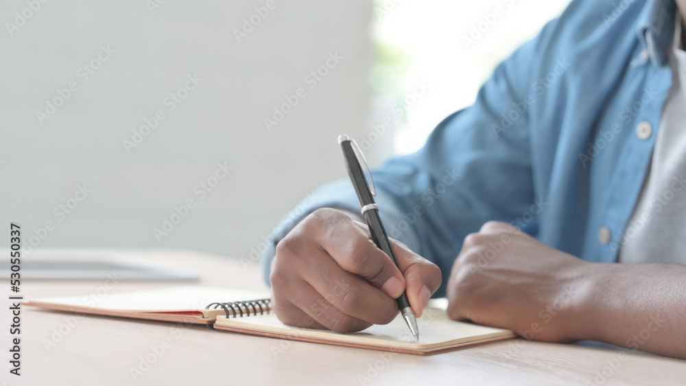 Close Up of Young African Man Writing on Notebook Close Up of Young African Man Writing on Notebook