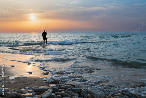 Young man fishing alone on the seashore at low tide at sunset.