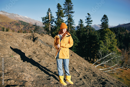 Woman hiking in the mountains walking and looking at the view of nature autumn in a yellow cape and hat full-length happiness