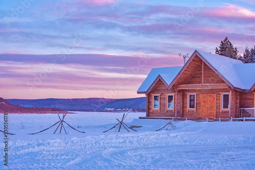 Beautiful shot of a wooden house in the snowy field in the sunset photo