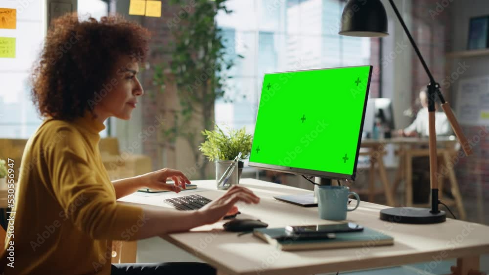 Portrait of a Happy Middle Eastern Manager Working in Creative Office. Business-Driven Stylish Female with Curly Hair Using Desktop Computer with Green Screen Mock Up Display.