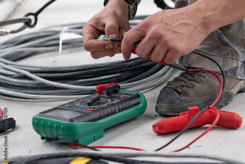 Close-up of an electrical engineer's hand ringing a cable with a multimeter or measuring voltage at a construction site.