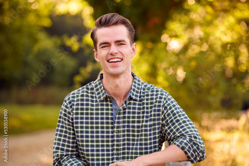 Portrait Of Casually Dressed Man Leaning On Fence On Walk In Countryside