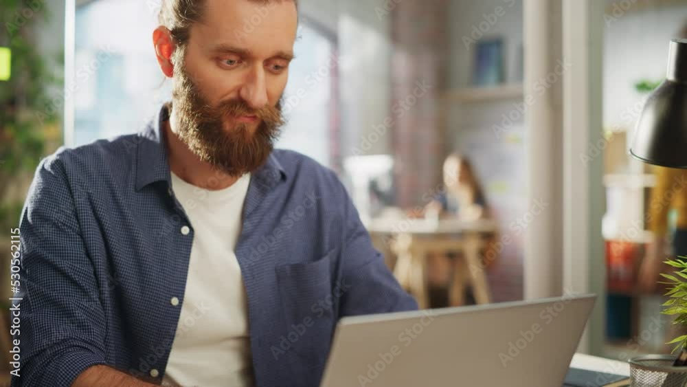 Close Up Portrait of a Handsome Long-Haired Bearded Manager Sitting at a Desk in Creative Office. Stylish Man Using Laptop Computer in Marketing Company. Writing Inspiring Startup Business Ideas. Close Up Portrait of a Handsome Long-Haired Bearded Manager Sitting at a Desk in Creative Office. Stylish Man Using Laptop Computer in Marketing Company. Writing Inspiring Startup Business Ideas.