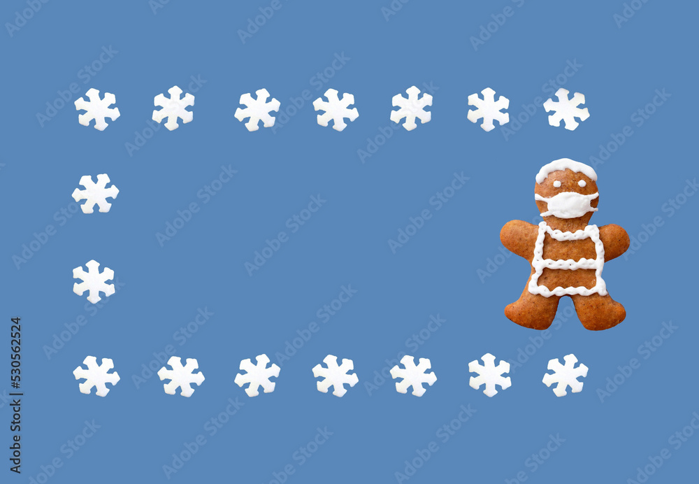 Gingerbread man with protective face mask in a frame from snowflakes, isolated, blue background. Greeting card, copy space for text. Creative concept in coronavirus (COVID-19) time