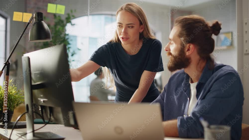 Two Stylish Employees Discussing Work-Related Projects on Computer in Creative Agency in Loft Office. Young Creative Director and Manager Talking About Work, Making Changes on Corporate Project.