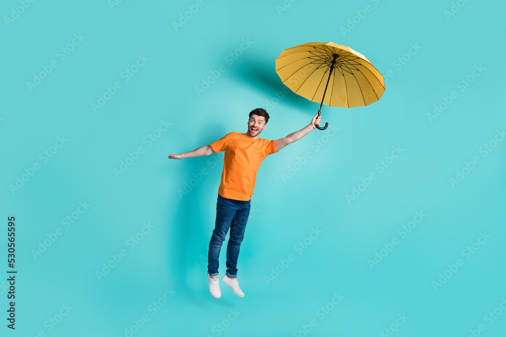 Full length photo of positive man dressed nice trendy outfit catch parasol fly empty space isolated on aquamarine color background Full length photo of positive man dressed nice trendy outfit catch parasol fly empty space isolated on aquamarine color background