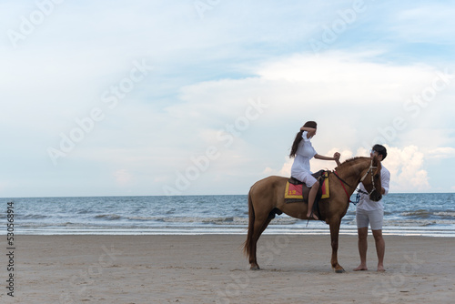 Young asian couple walking with horse on the beach in sunny summer day.