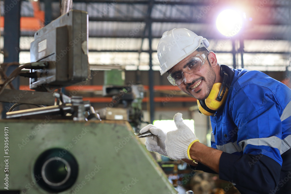 Technician engineer or worker man in protective uniform with safety hardhat maintenance operation or checking lathe metal machine at heavy industry manufacturing factory. Metalworking concept Technician engineer or worker man in protective uniform with safety hardhat maintenance operation or checking lathe metal machine at heavy industry manufacturing factory. Metalworking concept