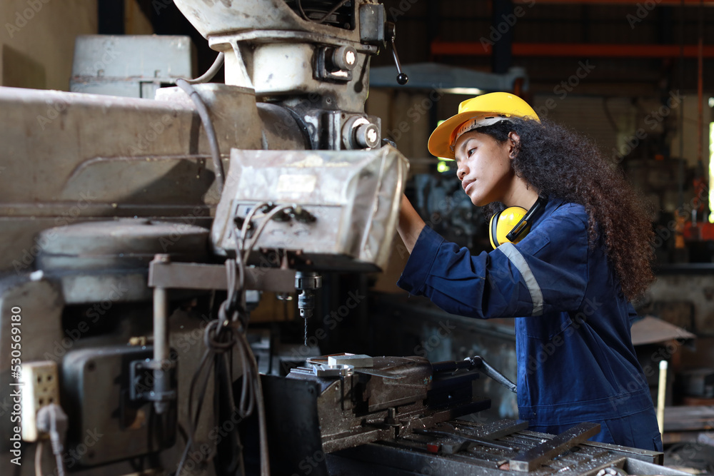 Technician engineer or worker woman in protective uniform with safety hardhat maintenance operation or checking lathe metal machine at heavy industry manufacturing factory. Metalworking concept