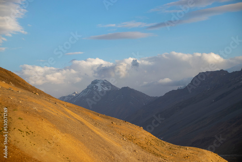 Sandy hill in Spiti Valley in front of white Himalayan peak surrounded by clouds
