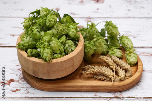 Fresh green hops and ears of wheat on white wooden table, closeup