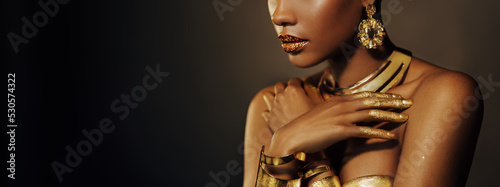 Portrait Closeup Beauty fantasy african woman, face in gold paint. Golden shiny black skin. Fashion model girl mixed race. Glamorous arab turban, jewellery accessories. Professional metallic makeup