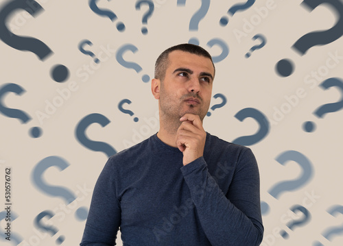 Close up photo of pensive and thoughtful man with the question marks on the backround. Concept of FAQ and mindblowing to find answer to questions. 