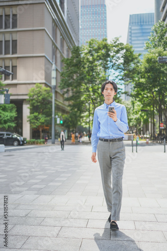 スマートフォンを操作しながらオフィス街を歩くビジネスマン