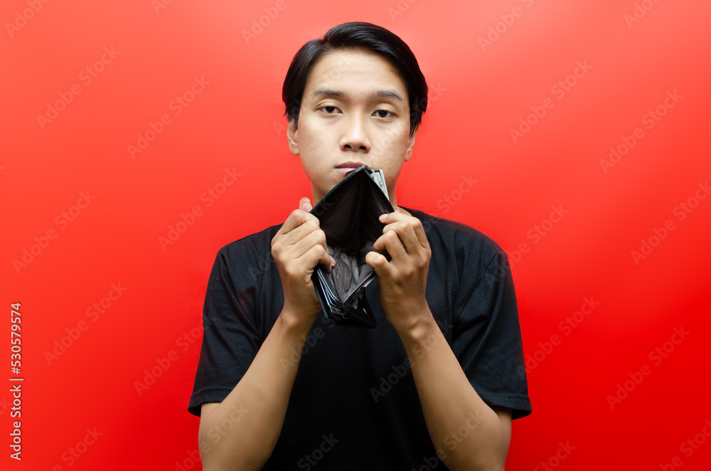 Portrait of sad asian man showing his empty wallet and looking at camera isolated over red background. bankrupt concept. jobless concept. Portrait of sad asian man showing his empty wallet and looking at camera isolated over red background. bankrupt concept. jobless concept.