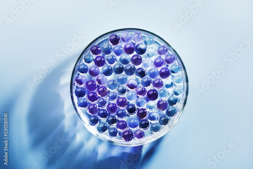 Sample of gel bubbles in petri dish on blue background, hard shadows. Abstract science, medicine and beauty concept