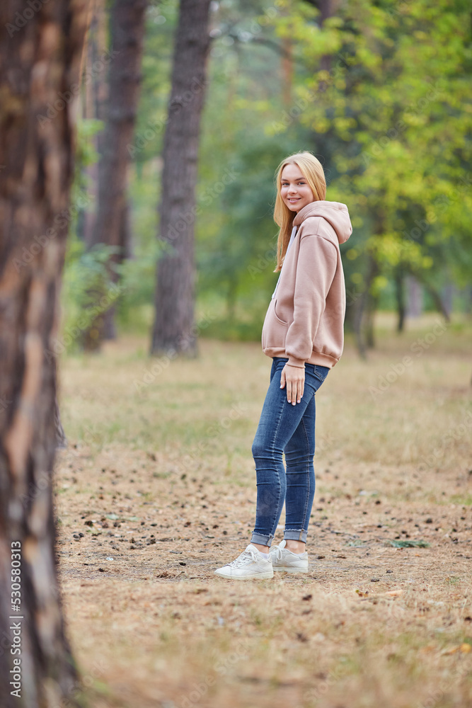 Attractive blue eyed blonde woman walk on the city park. Girl wear beige hoodie, pink bag and look happy and smiles. Attractive blue eyed blonde woman walk on the city park. Girl wear beige hoodie, pink bag and look happy and smiles.
