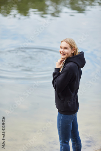 Beautiful young blonde woman in black hoodie walks in the park. Attractive female spending active time in the park.