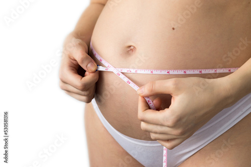 young pregnat woman measuring growing belly with a imperial system tape