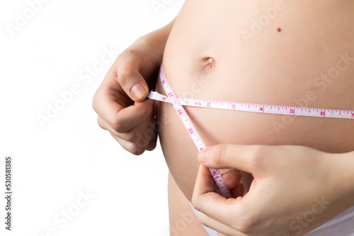 young pregnat woman measuring growing belly with a imperial system tape