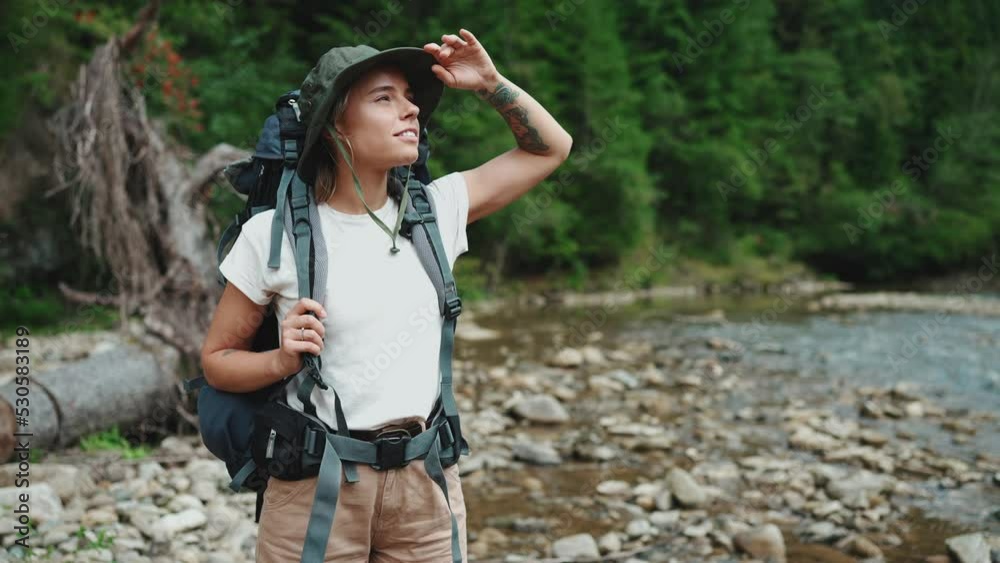Handsome blonde tourist woman looking around near river in the mountains Handsome blonde tourist woman looking around near river in the mountains