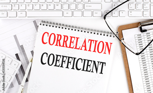 Text CORRELATION COEFFICIENT on Office desk table with keyboard, notepad and analysis chart on white background. photo
