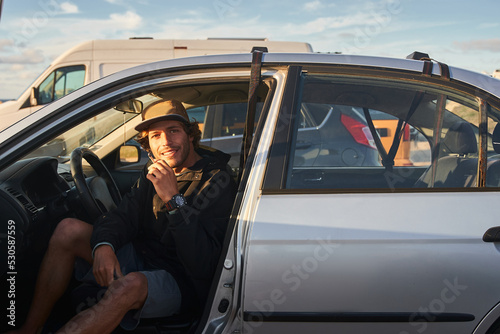 Handsome young man smoking hand rolled cigarette while sitting at the car at the beach photo