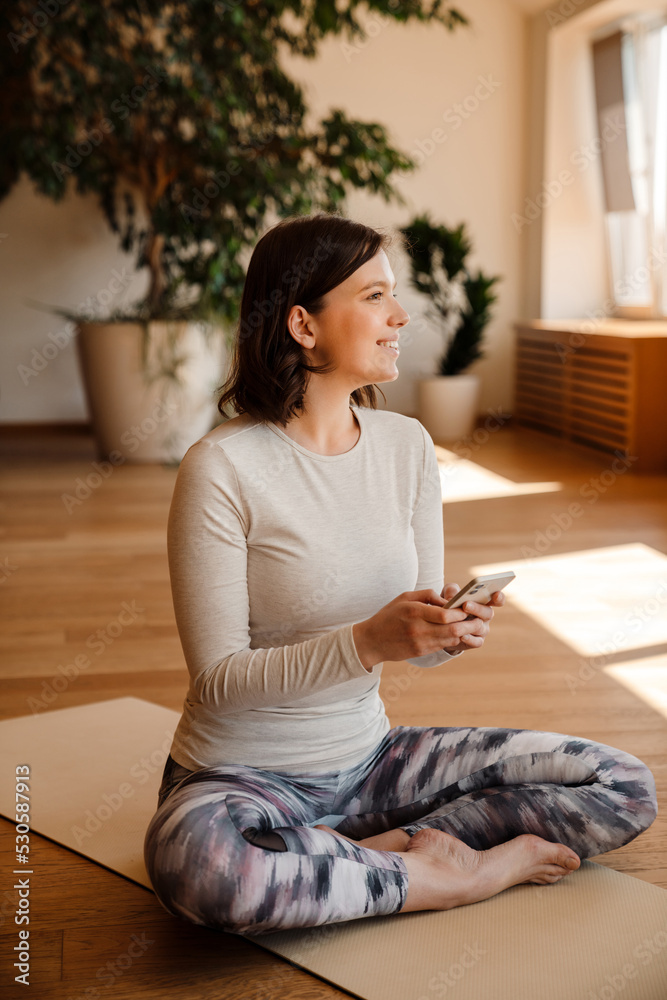 Young white woman smiling and using mobile phone during yoga class