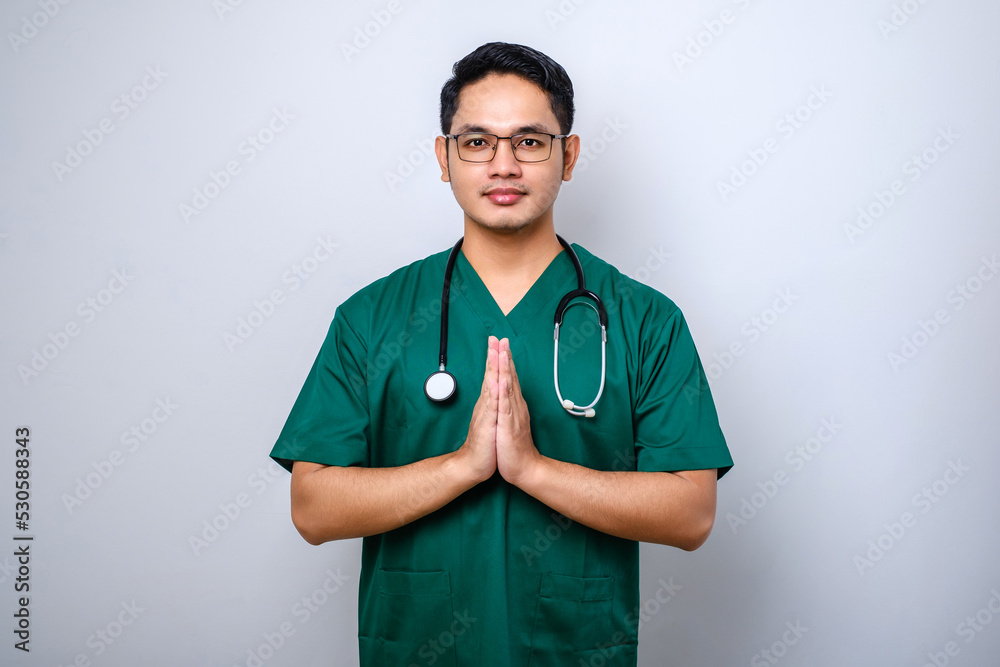 Smiling beautiful asian male doctor, physician in scrubs smiling greeting gesture isolated white background Smiling beautiful asian male doctor, physician in scrubs smiling greeting gesture isolated white background