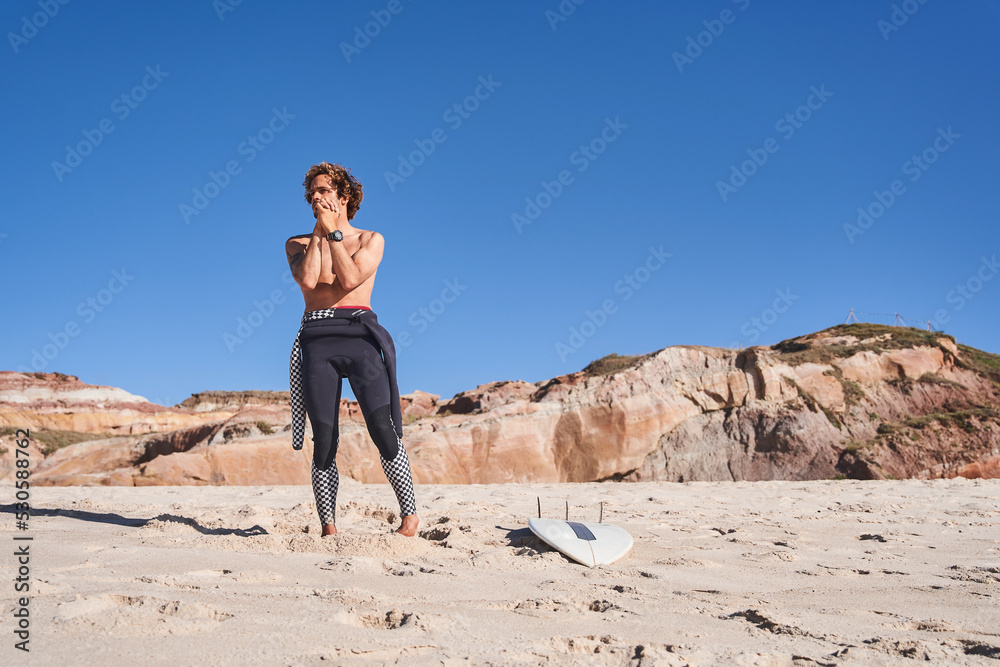 Athletic man stretching arms before surfing and training at the beach