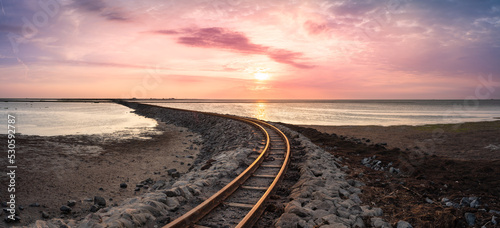 Sonnenuntergang und Damm mit Gleis an der deutschen Nordseeküste im Wattenmeer Richtung 
