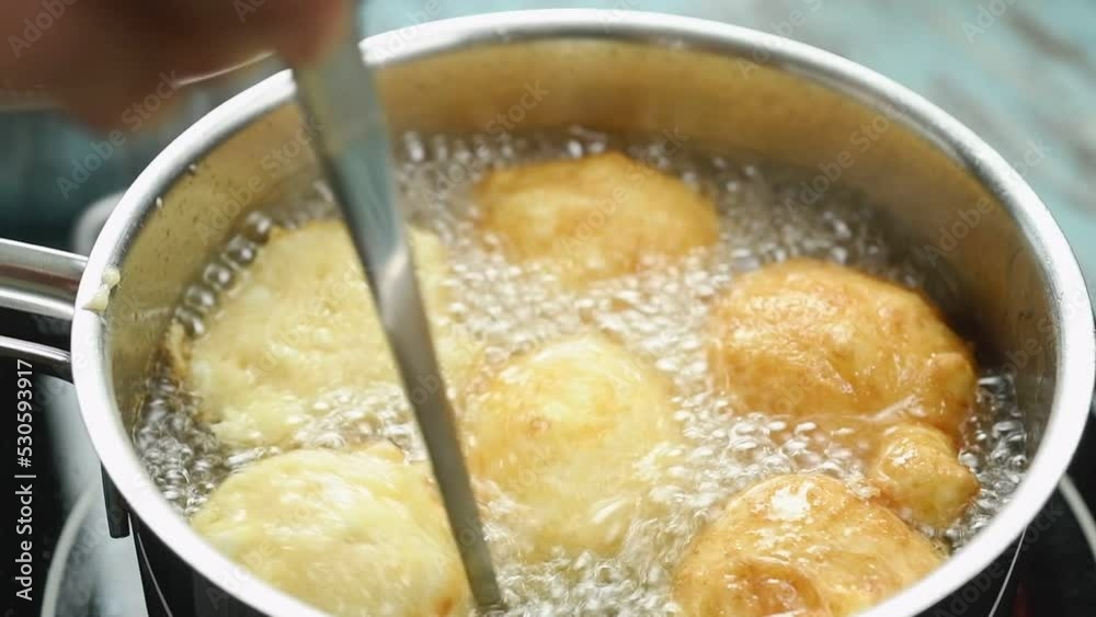 The chef flips the donuts in the pan of oil to fry them.
The chef flips the donuts in the pan of oil to fry them.