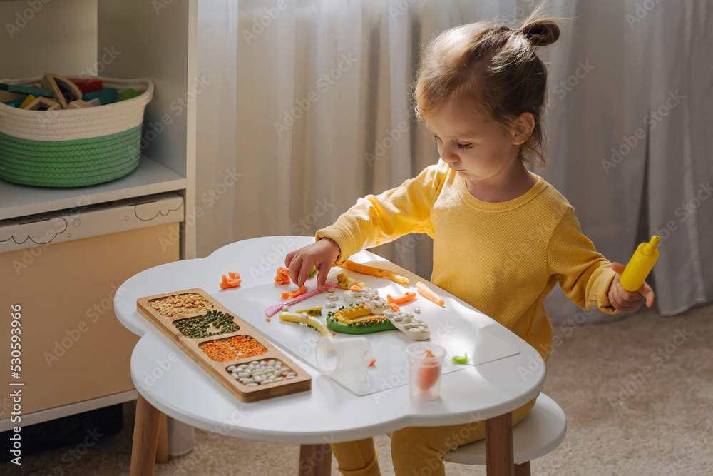A little girl playing with rainbow from play dough for modeling with decorate from dried beans