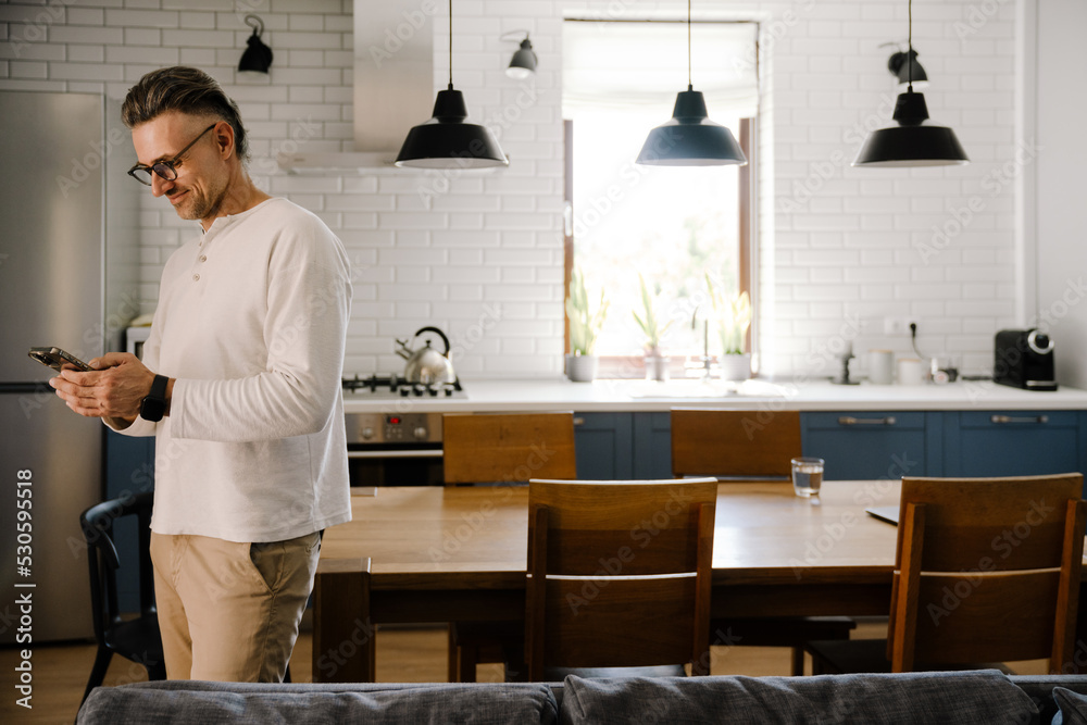 Fototapeta premium White mid man smiling and using mobile phone at home