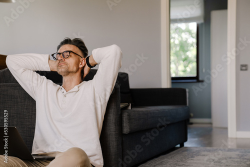 White man smiling and using laptop while sitting on floor at home