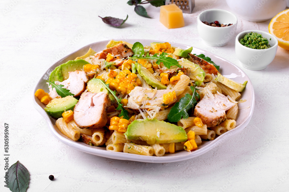 Pasta salad with chicken, avocado, grilled corn, cheese, arugula and pesto sauce served on the white plate Pasta salad with chicken, avocado, grilled corn, cheese, arugula and pesto sauce served on the white plate