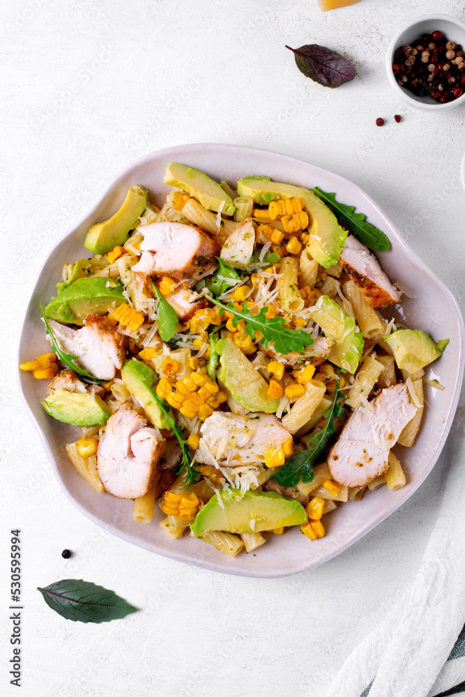 Pasta salad with chicken, avocado, grilled corn, cheese, arugula and pesto sauce served on the white plate. Top view