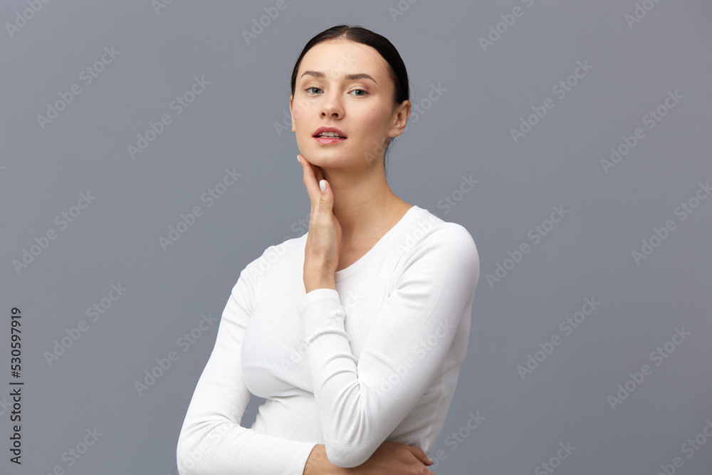 an excited woman stands on a gray background in a white T-shirt, carefully put her hand to her ear, lowering the second on her stomach an excited woman stands on a gray background in a white T-shirt, carefully put her hand to her ear, lowering the second on her stomach