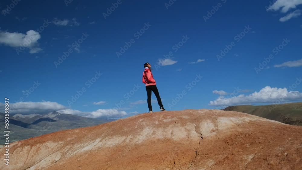 Happy inspired female tourist standing against the background of mountains and blue sky. Young woman admires stunning panorama. Dynamic camera. Happy inspired female tourist standing against the background of mountains and blue sky. Young woman admires stunning panorama. Dynamic camera.