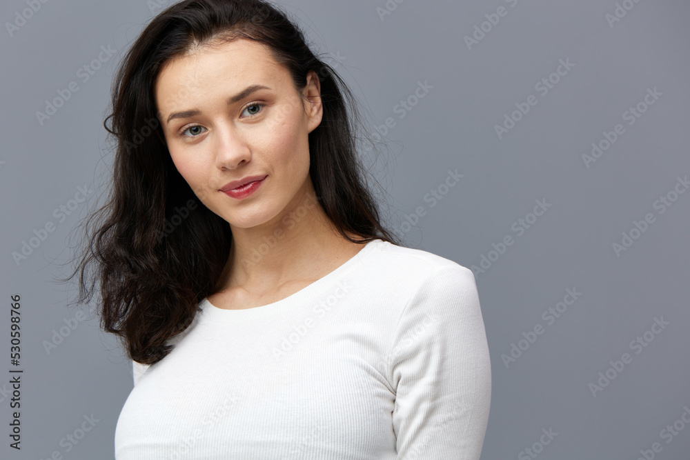 an excited woman stands on a gray background in a white T-shirt, gently looking forward with a slight smile an excited woman stands on a gray background in a white T-shirt, gently looking forward with a slight smile