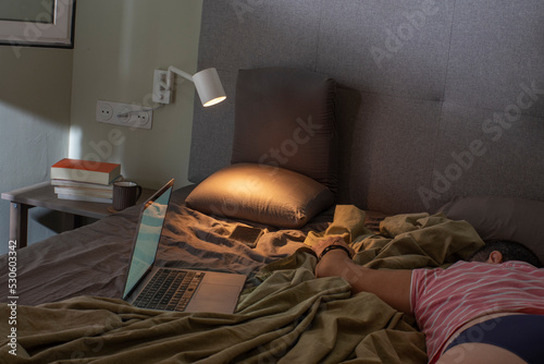 habitación y cama con ordenador, en la mesita libros. Mujer estirada durmiendo del cansancio, concepto de exceso de trabajo, trabajo para casa photo