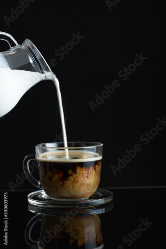 Coffee with cream. Pouring the cream from the pitcher into the coffee. Black background. Copy Space.