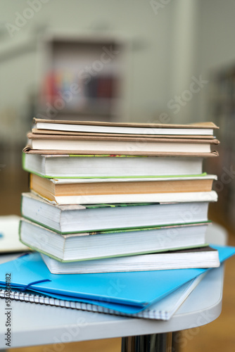 Vertical shot of the book stack on wood desk and blurred bookshelf in the library room, education background. Back to school concept
